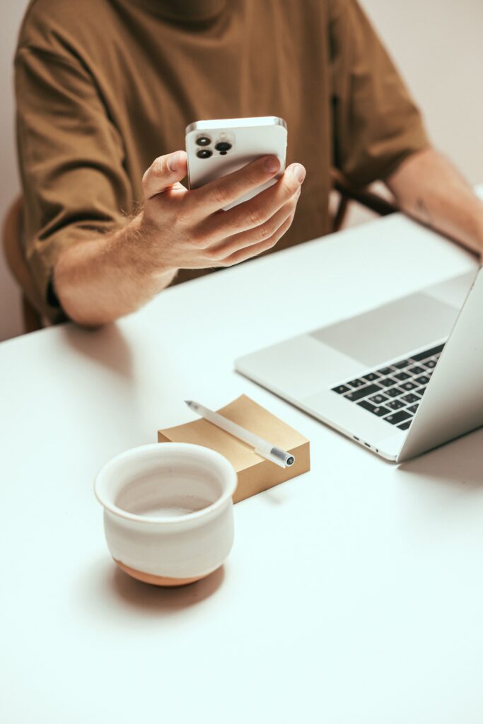 Person interacting with smartphone at tidy desk with laptop and coffee mug, showcasing modern technology.